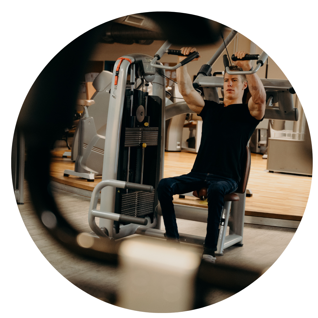 Strength Training on Gym Machine » PEMF Recovery Plus Young man working out on a seated gym weight machine targeting upper body strength.