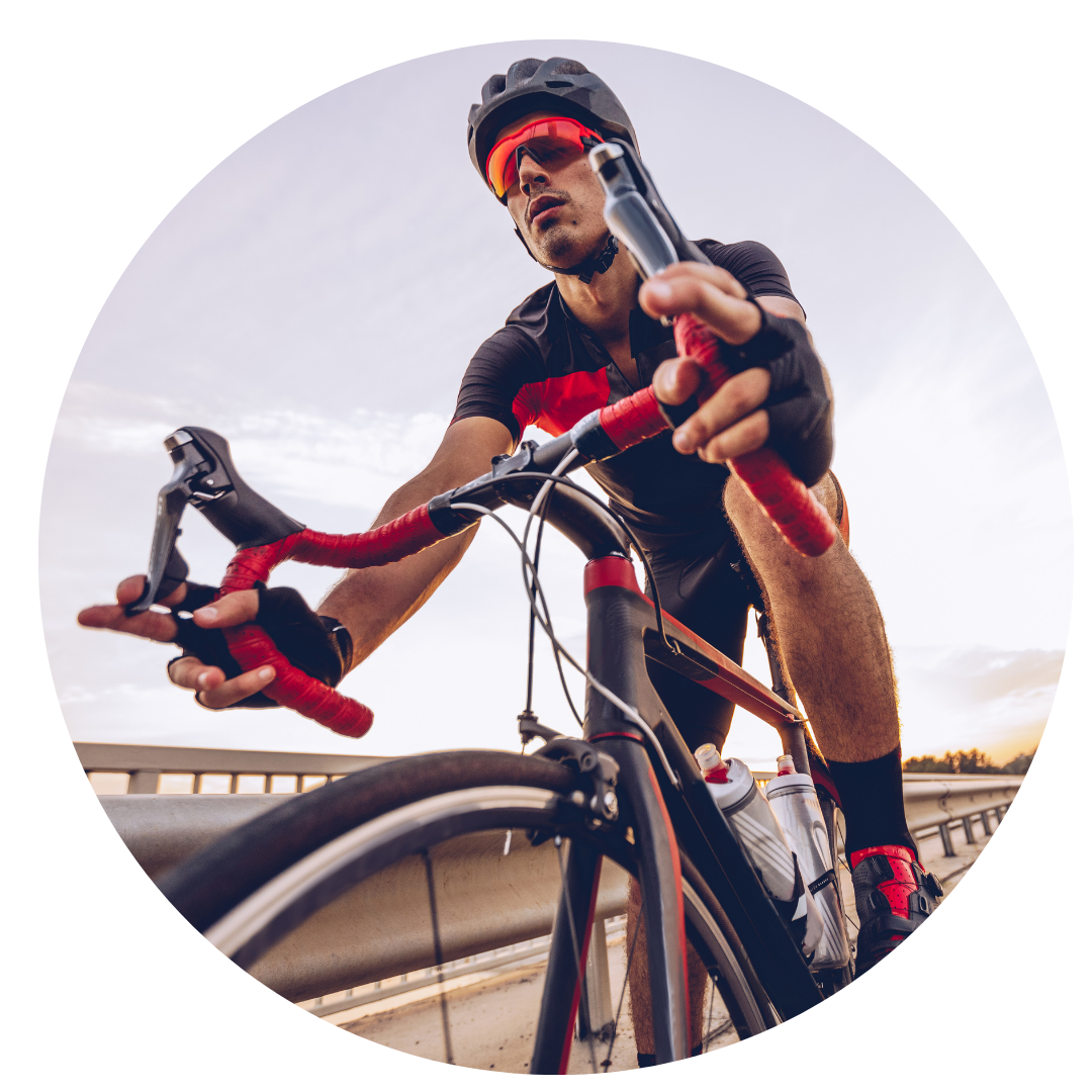 Endurance Cyclist on Road Bike » PEMF Recovery Plus Focused male cyclist in gear pedaling on a road bike across a bridge during a training session.