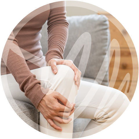 Knee Joint Discomfort in Daily Life » PEMF Recovery Plus Woman seated on couch holding her knee in pain, indicating joint discomfort.