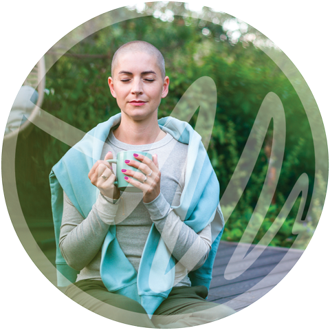 Woman with a shaved head calmly meditating outdoors with a mug, symbolizing cancer recovery.