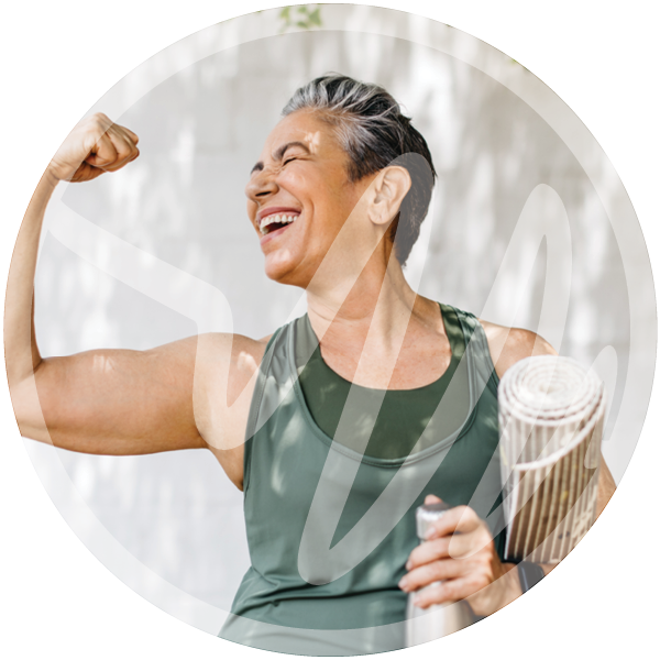 Confident Senior Woman Flexing After Yoga » PEMF Recovery Plus Happy senior woman in athletic wear flexing her arm and holding a yoga mat and water bottle, showing strength and confidence.